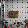 Brown leather Standard Issue Leather Case hanging on a pegboard wall above wrenches and pliers